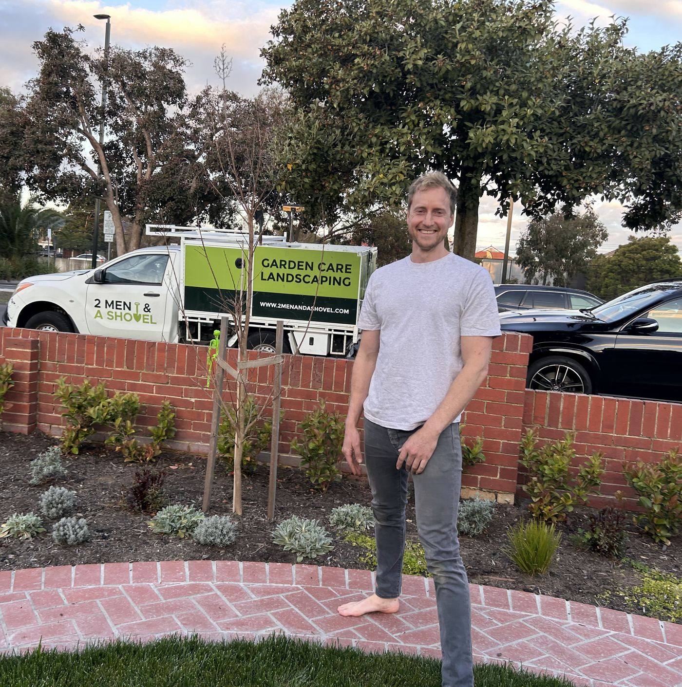 Andy from 2 Men and a Shovel standing in a freshly planted garden, his ute parked behind the brick wall